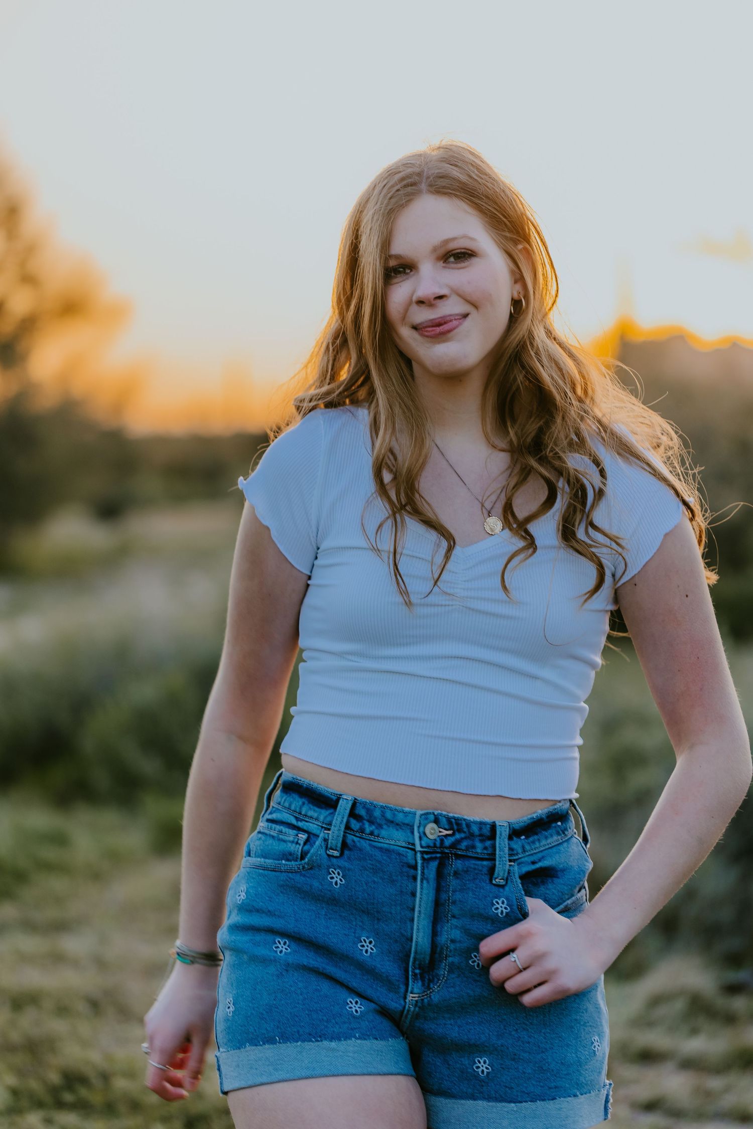 Casual outdoor portrait with person wearing blue crop top and jean shorts against natural backdrop.
