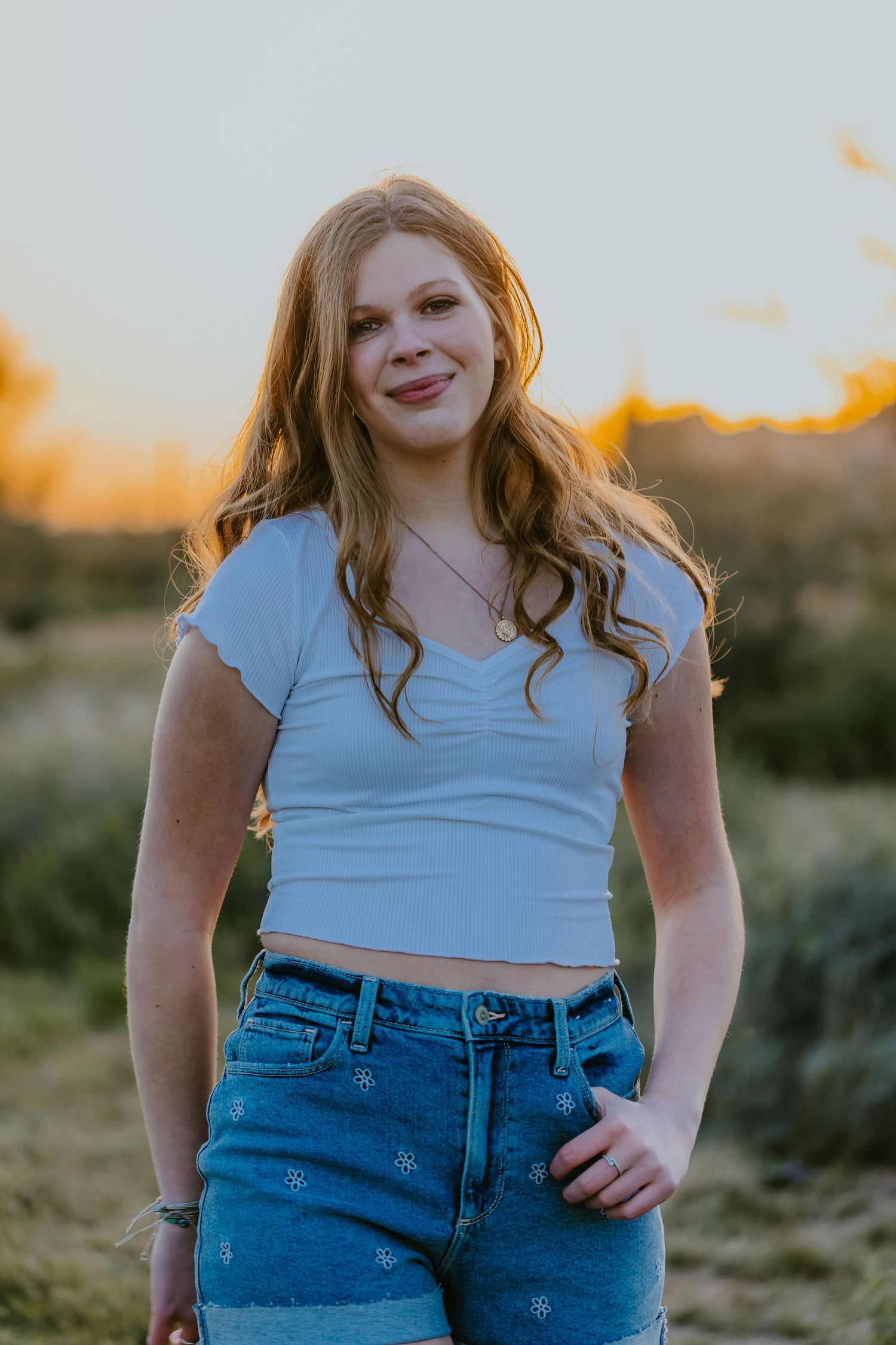 Person in summer attire smiling at camera with sunset glow in background.