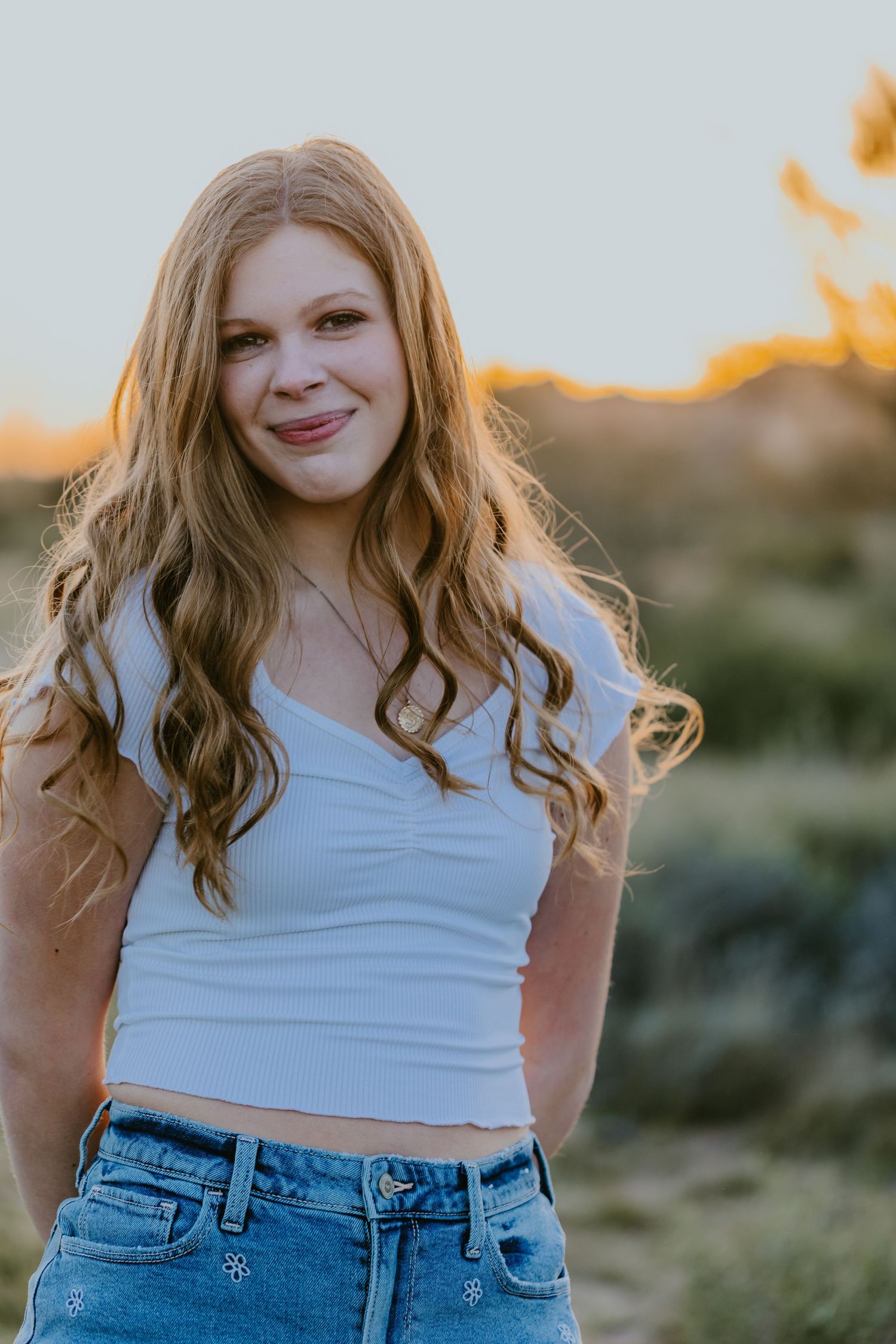 Person wearing white crop top and denim shorts smiling during outdoor photoshoot.