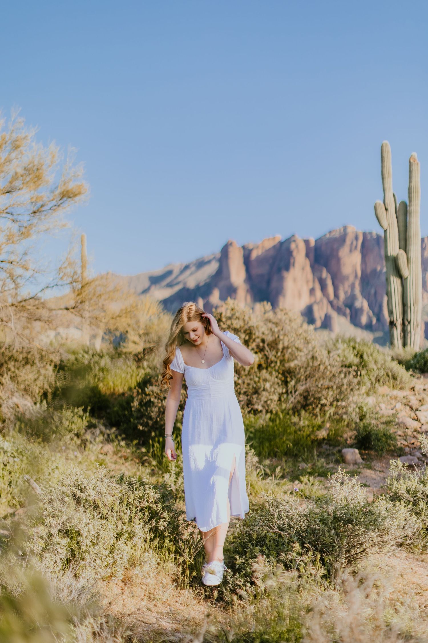 A flowing white sundress contrasts beautifully with the rugged desert landscape and majestic saguaros.