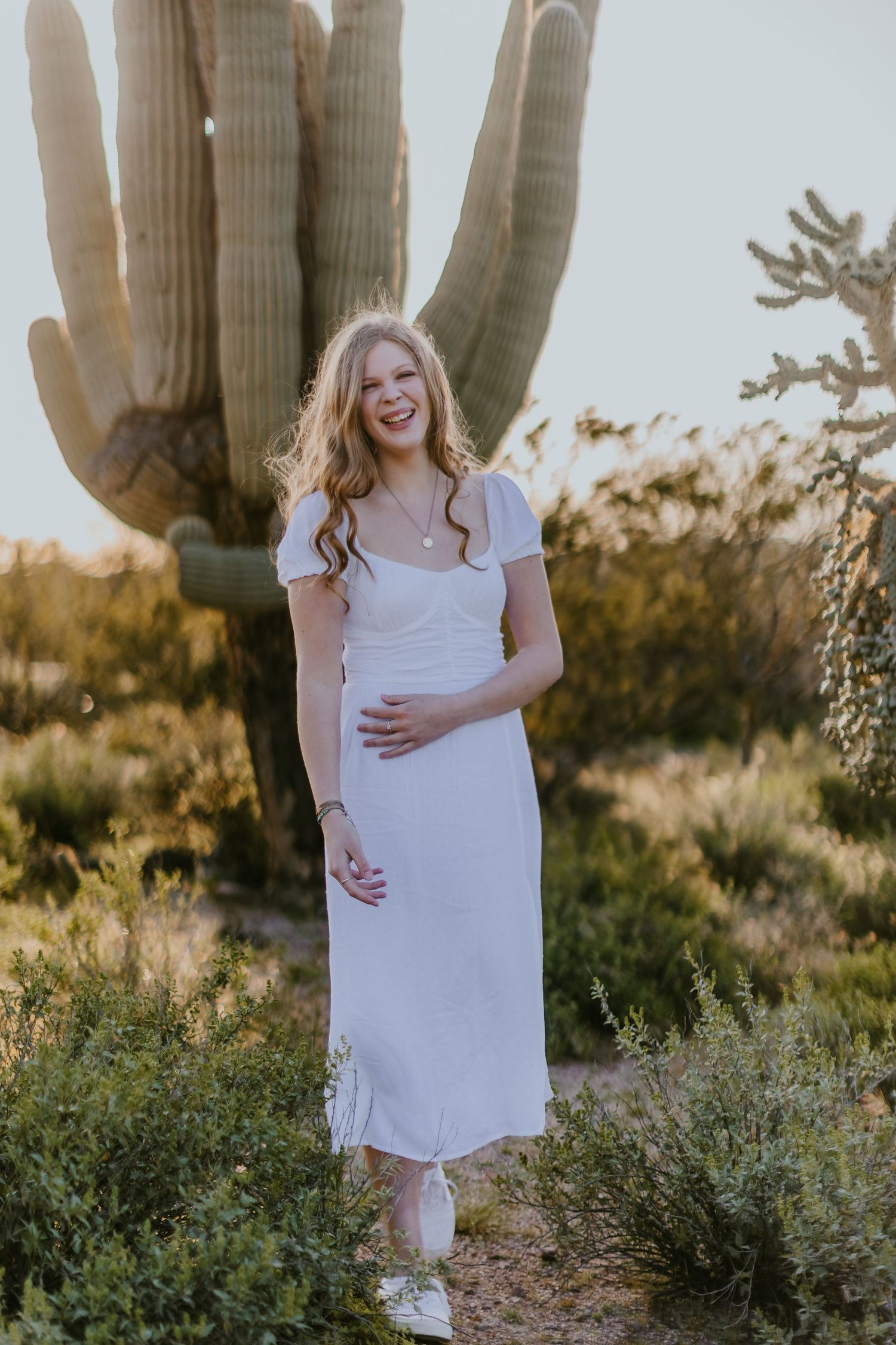 Gentle desert breeze catches white dress near majestic saguaro cactus at golden hour.