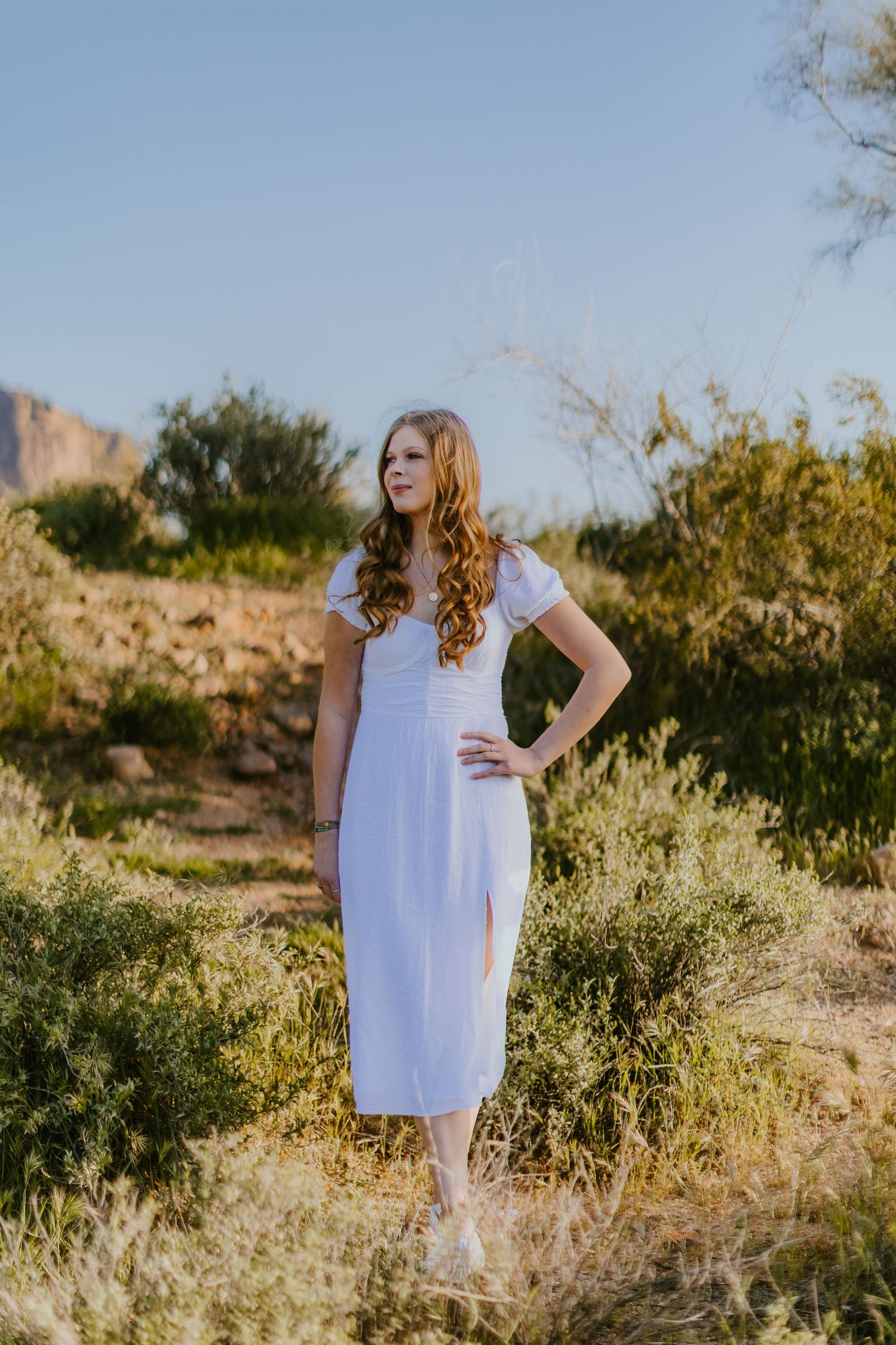 Person in white dress posing among desert vegetation during golden hour.