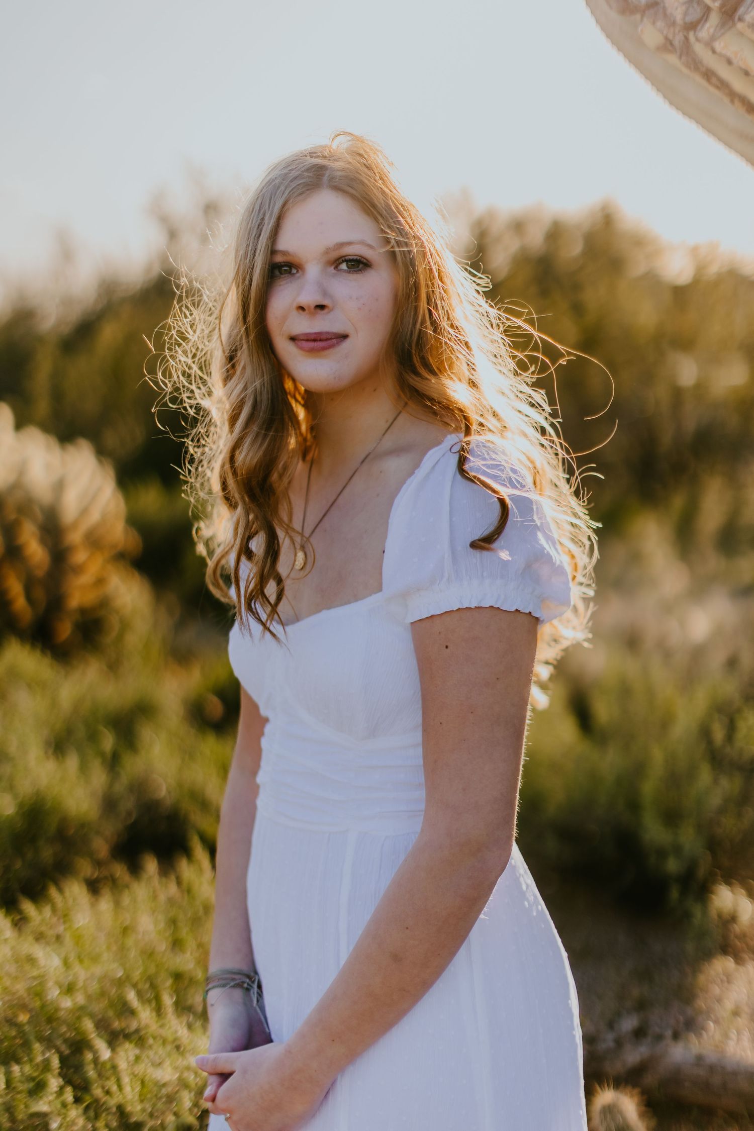 A white dress portrait in golden sunlight with desert foliage in the background.