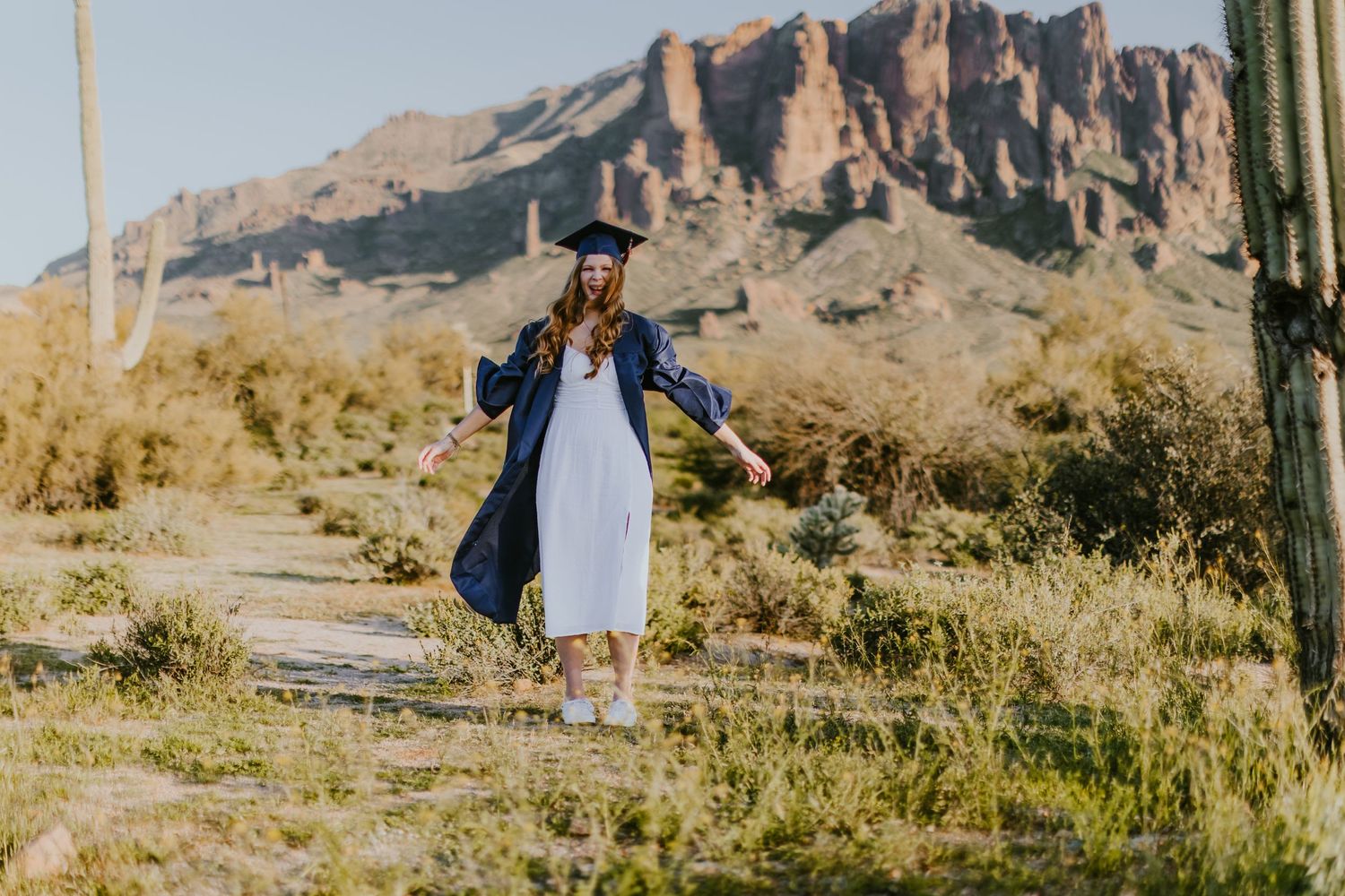Graduate walking along desert trail with majestic mountain backdrop.