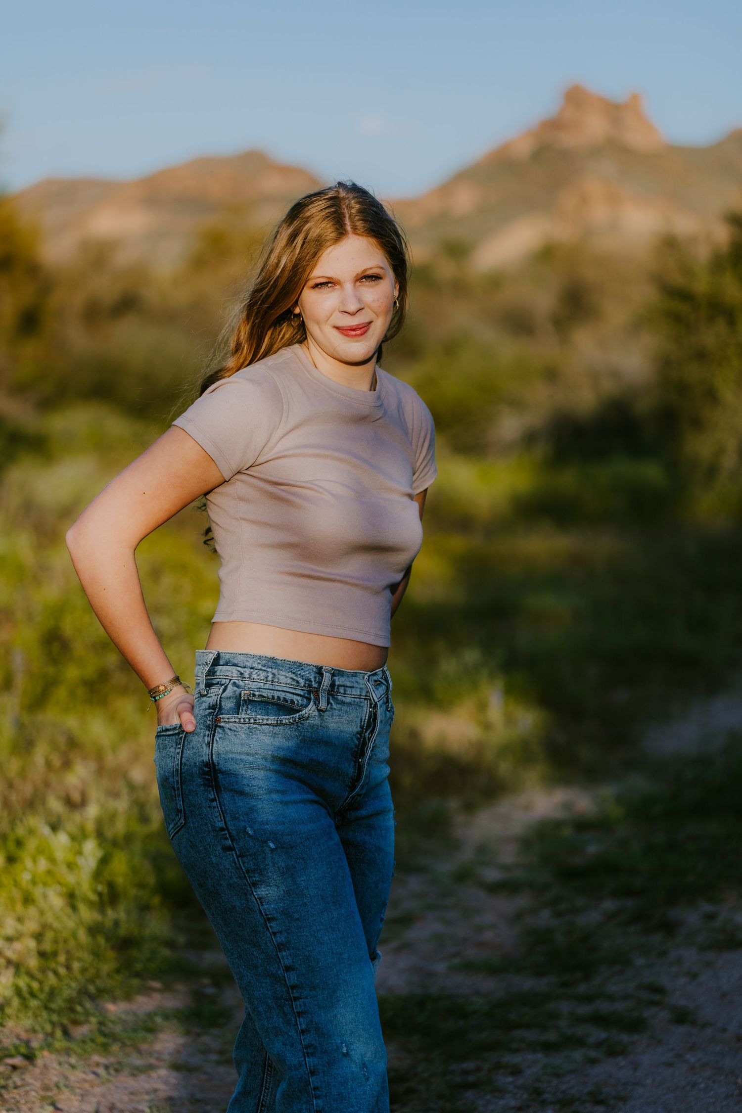 Warm evening light illuminates casual outfit with beige top and denim on mountain trail.
