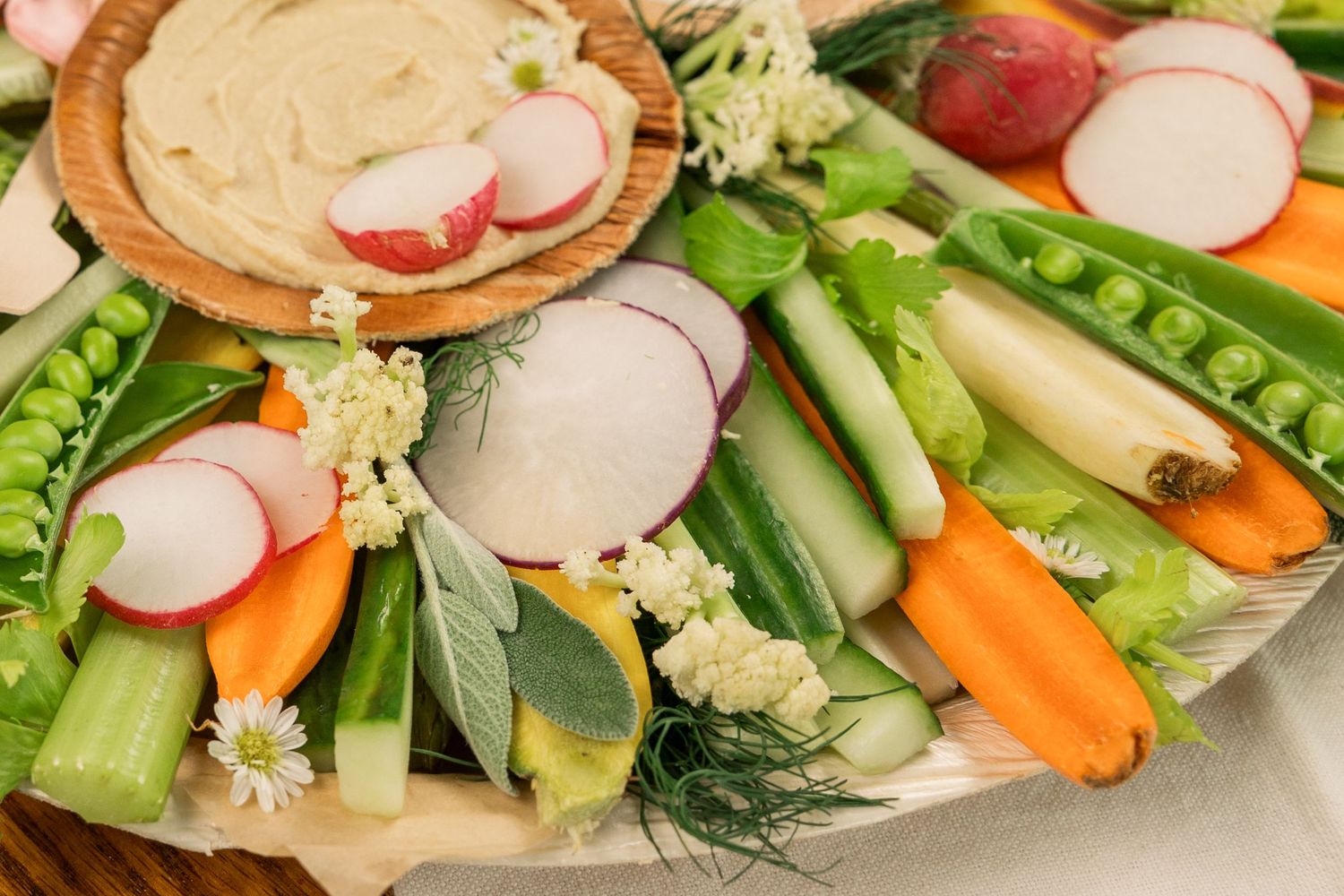 Fresh vegetable platter with radishes, carrots, celery and creamy dip in wooden bowls.