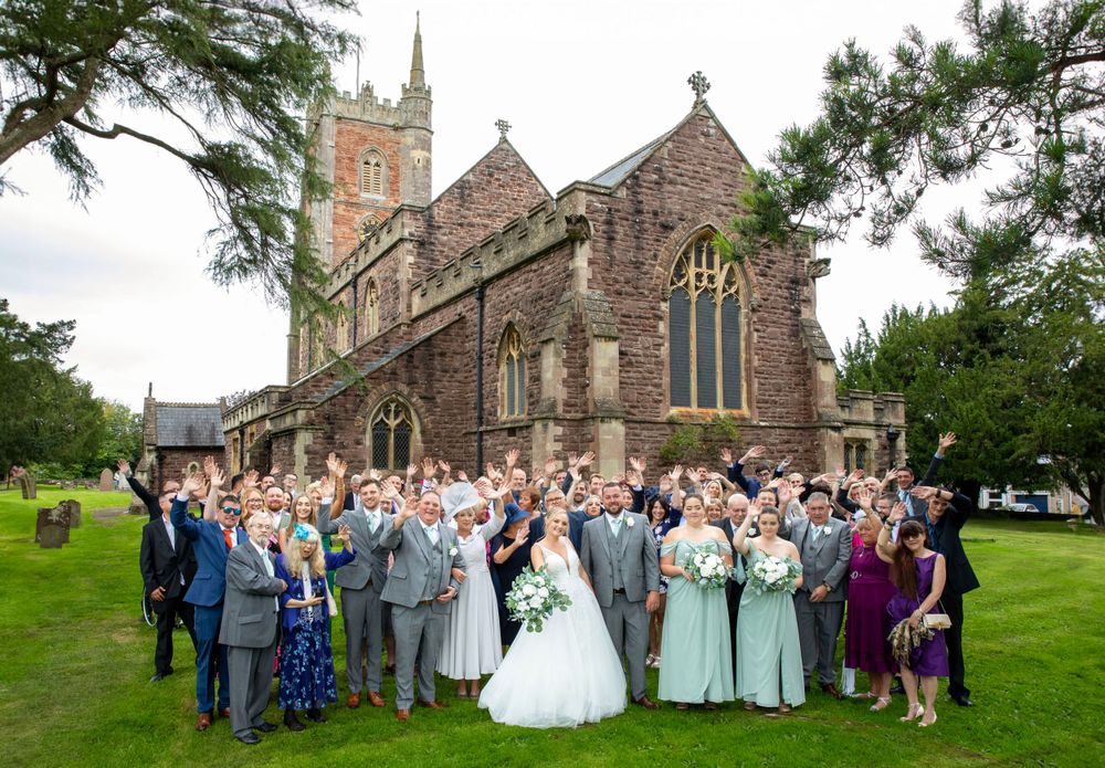Group shot of wedding and guests in church grounds.