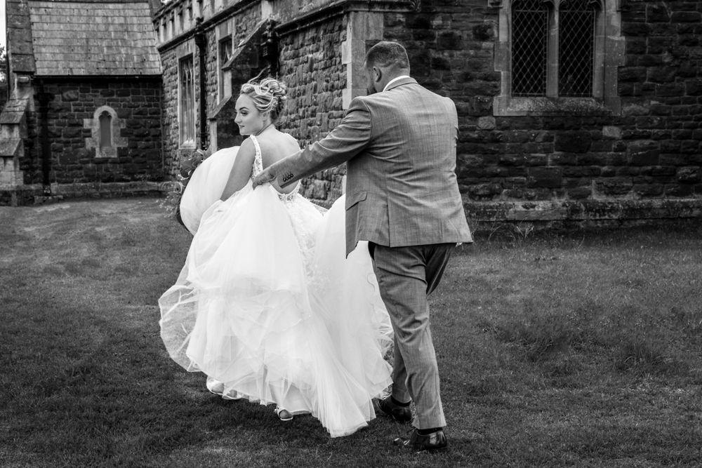 Bride and groom, black and white shot. Groom carrying bride dress.