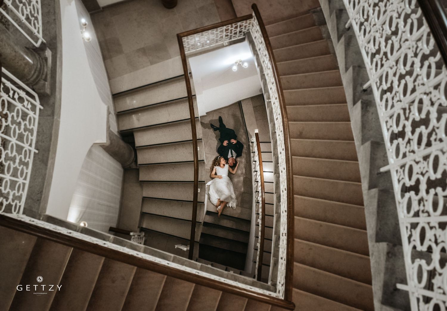 A creative spiral staircase wedding photo shot from above showing flowing white dress.