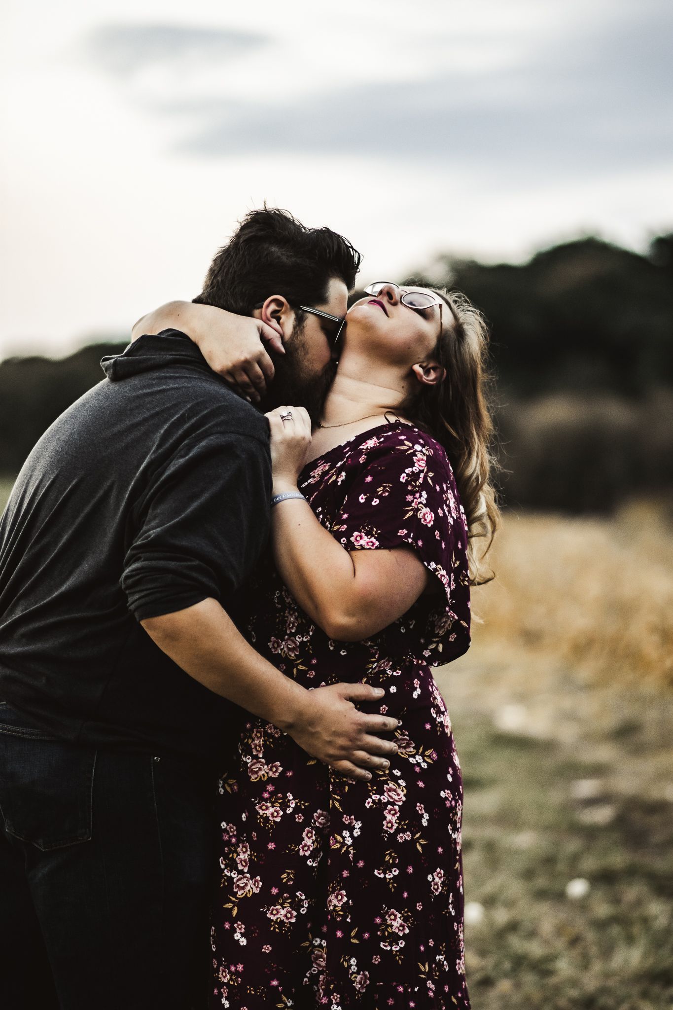 Romantic couple in casual attire sharing an intimate embrace in a rustic field setting.