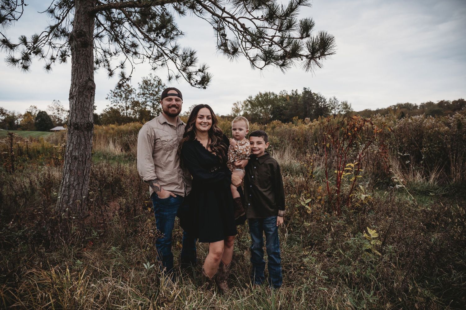 A group of people pose together in an outdoor autumn setting surrounded by rustic natural scenery and pine trees.