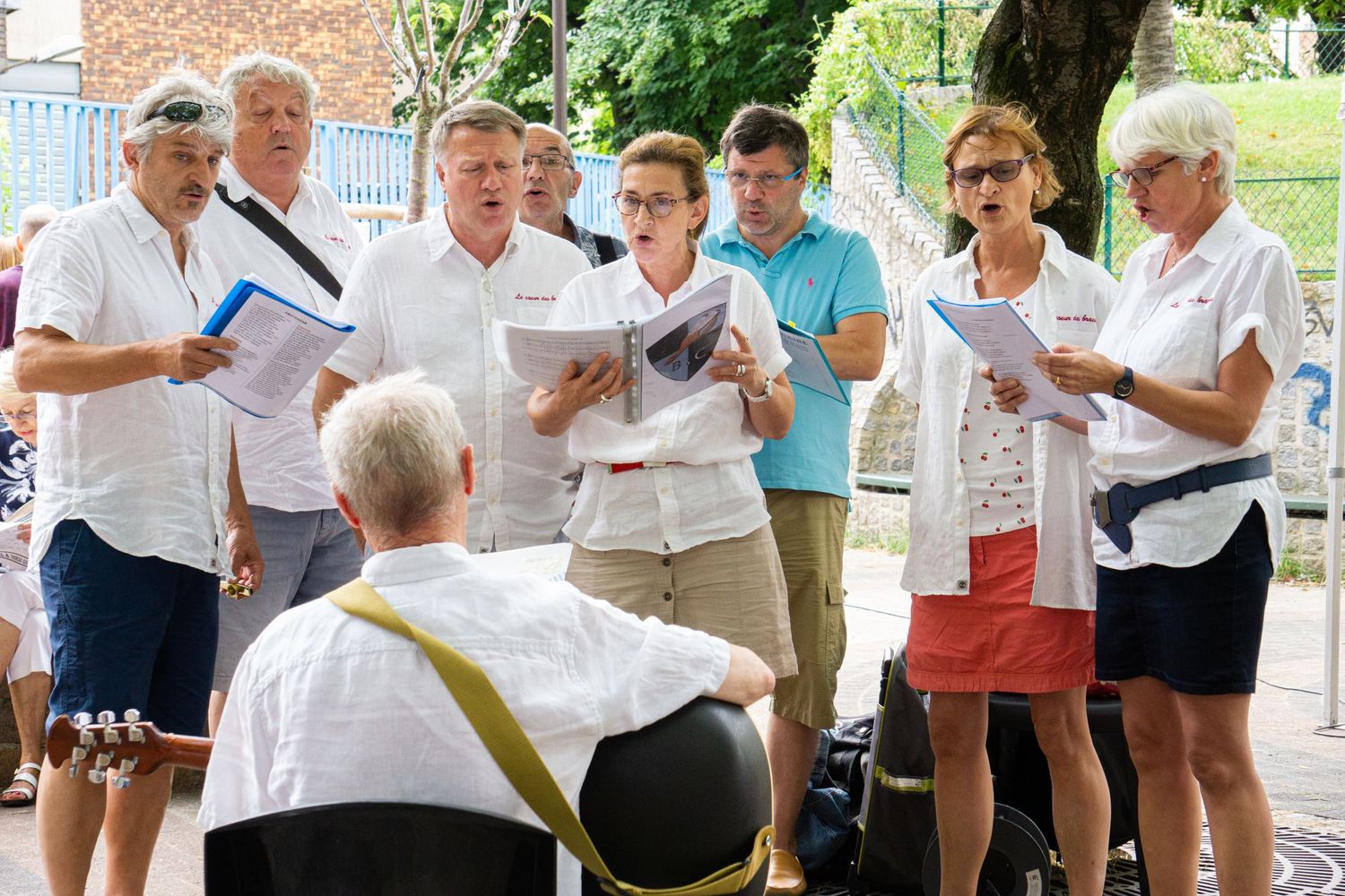 Group of people in white shirts holding papers outdoors during a gathering.