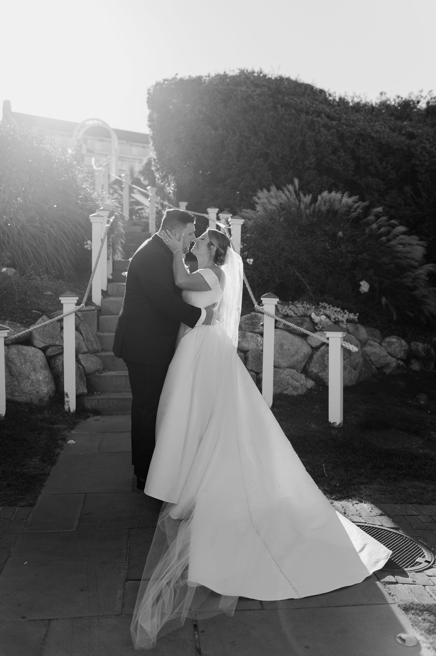 Black and white wedding photo captures couple's first dance under outdoor pergola.