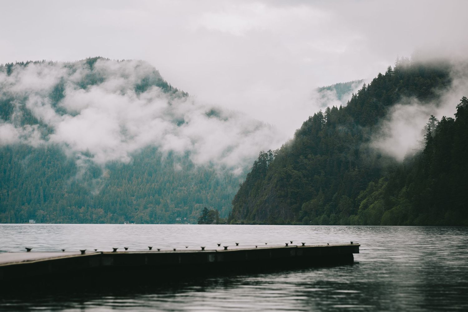 A landscape of a dock on lake crescent. Mountains in the background.