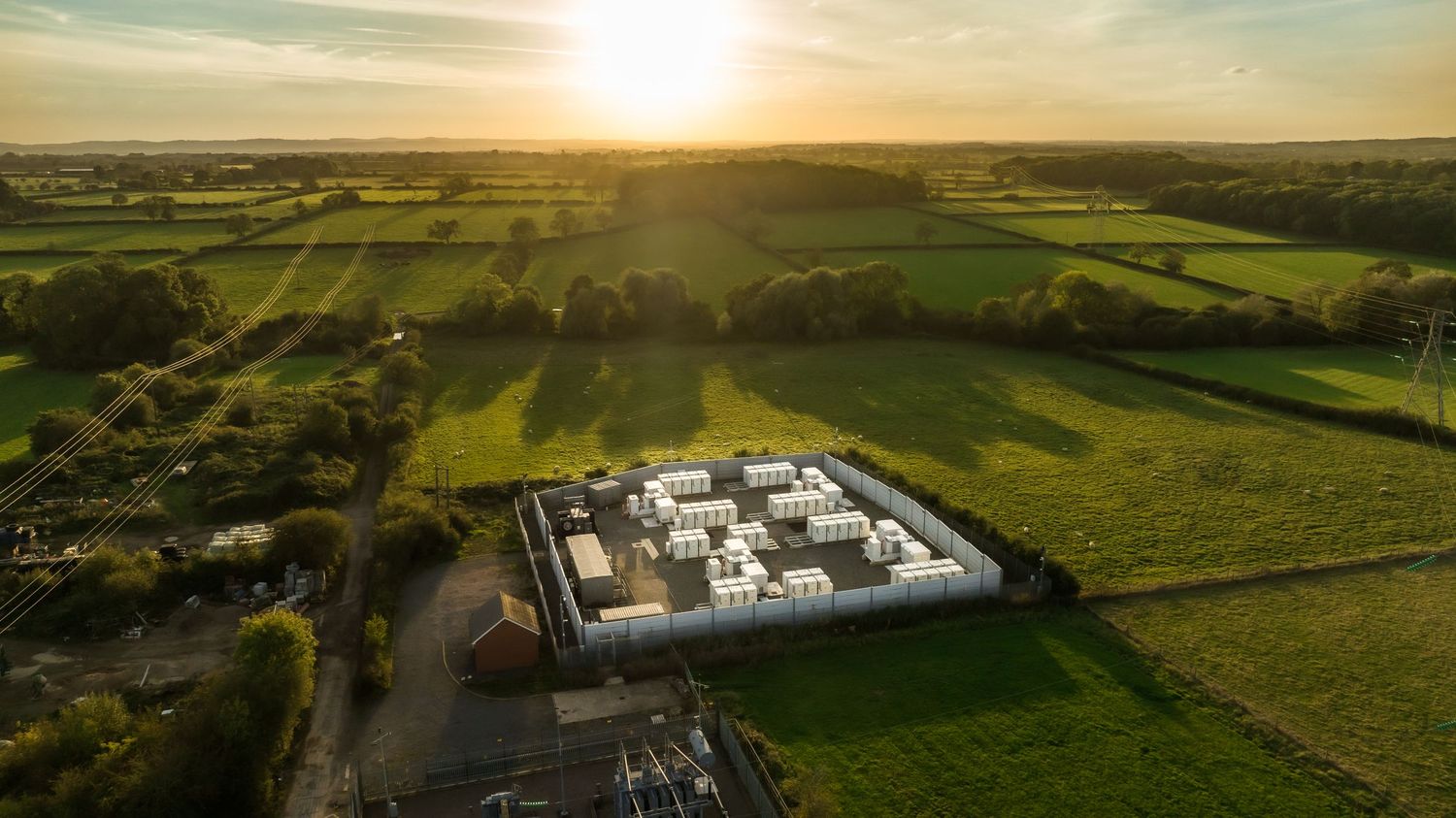 Aerial view of a modern white building complex surrounded by lush green fields at sunset.