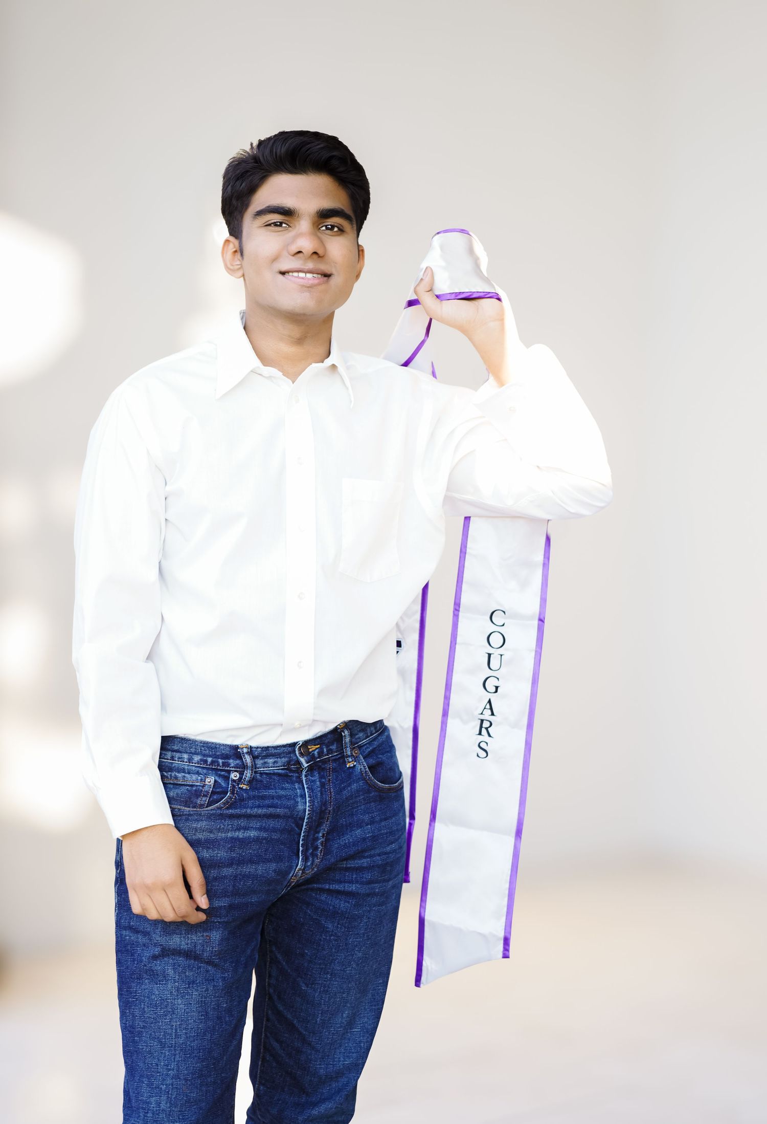 Young man in white shirt and jeans holding up a large purple crutch or medical device against white background.