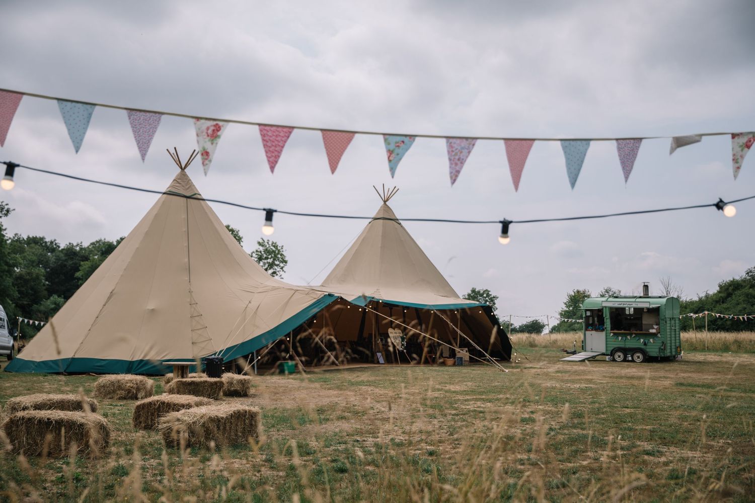 Festival-style teepee tents with bunting and string lights decorating an outdoor event space.