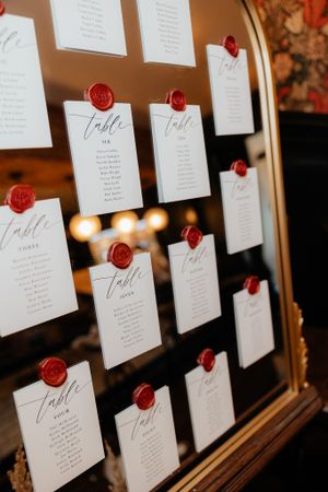Wedding seating chart displayed on dark background with white cards secured by red wax seals.