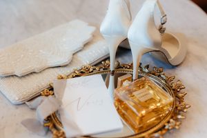 Elegant bridal accessories including white shoes and golden decorative elements on dark surface.