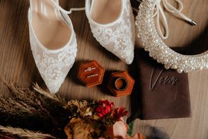 Elegant wedding shoes and accessories arranged with dried flowers and vintage details on a wooden surface.