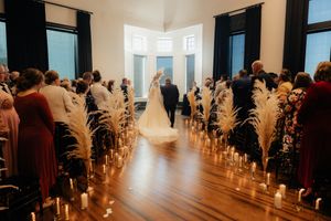 Guests gather in an elegant indoor venue decorated with white floral arrangements and candlelight for a wedding ceremony.