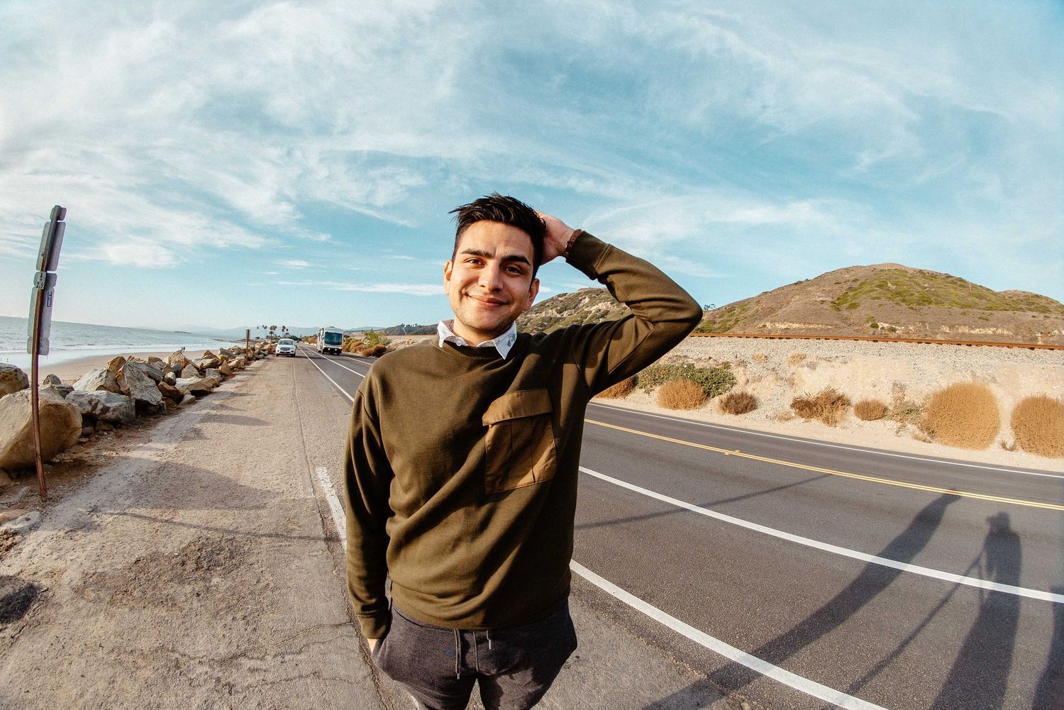 Person standing on an empty desert highway with mountains in the background.