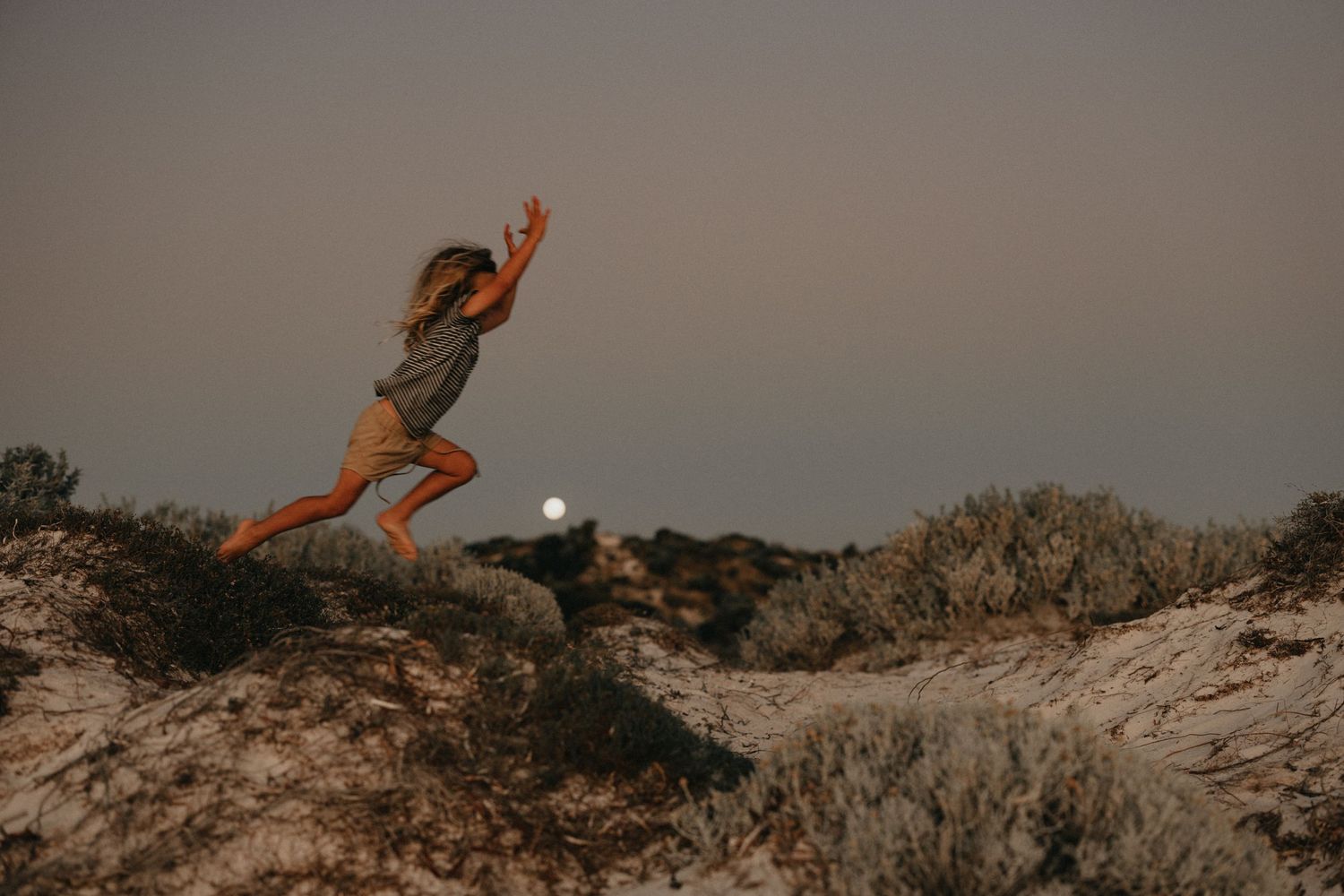 Person leaping gracefully over rocks at sunset against a moody sky.