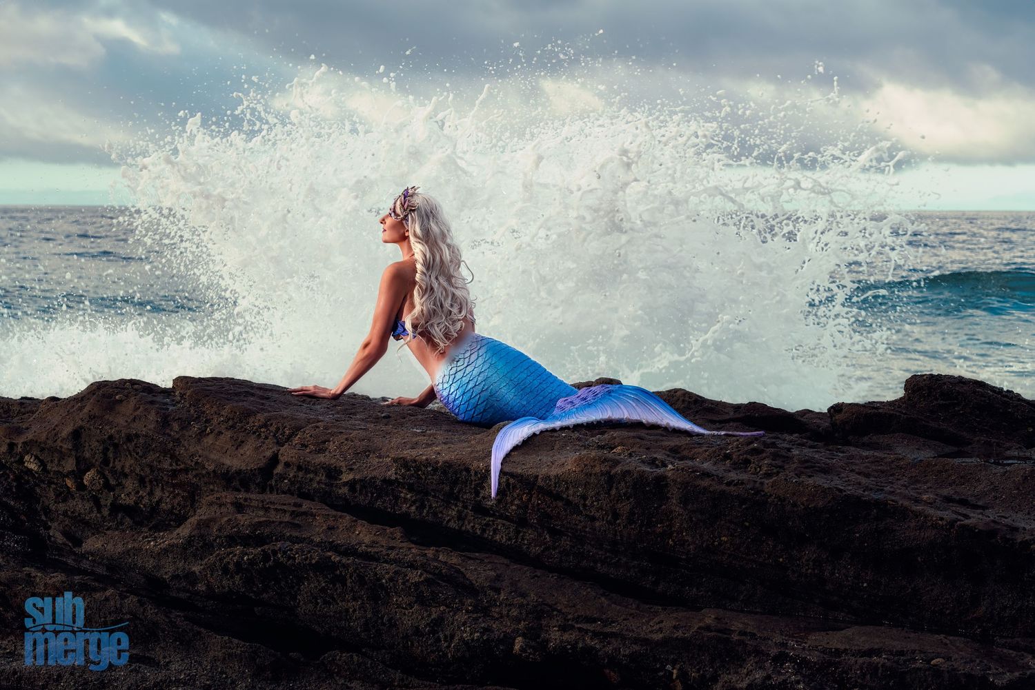 Mermaid costume photo with ocean waves crashing dramatically on rocky shore.