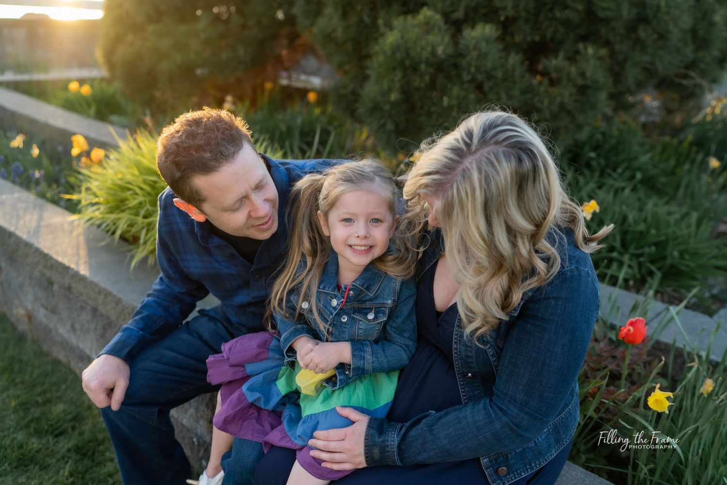 Family laughing together during sunset photo session in a garden.