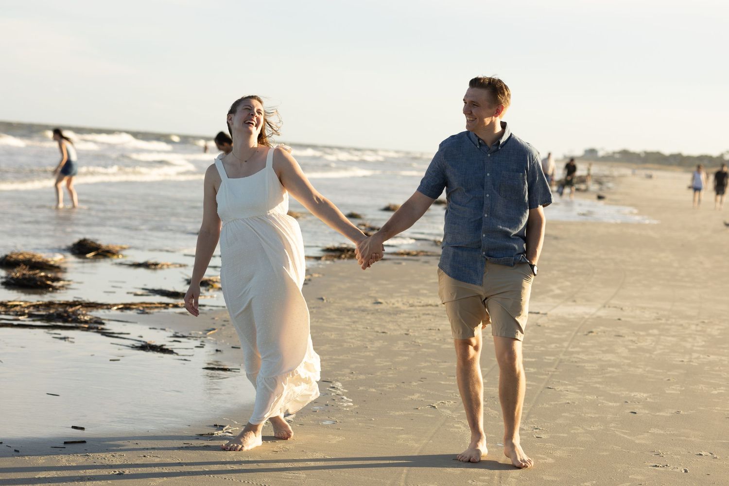 Couple walking hand in hand along a beach at sunset.