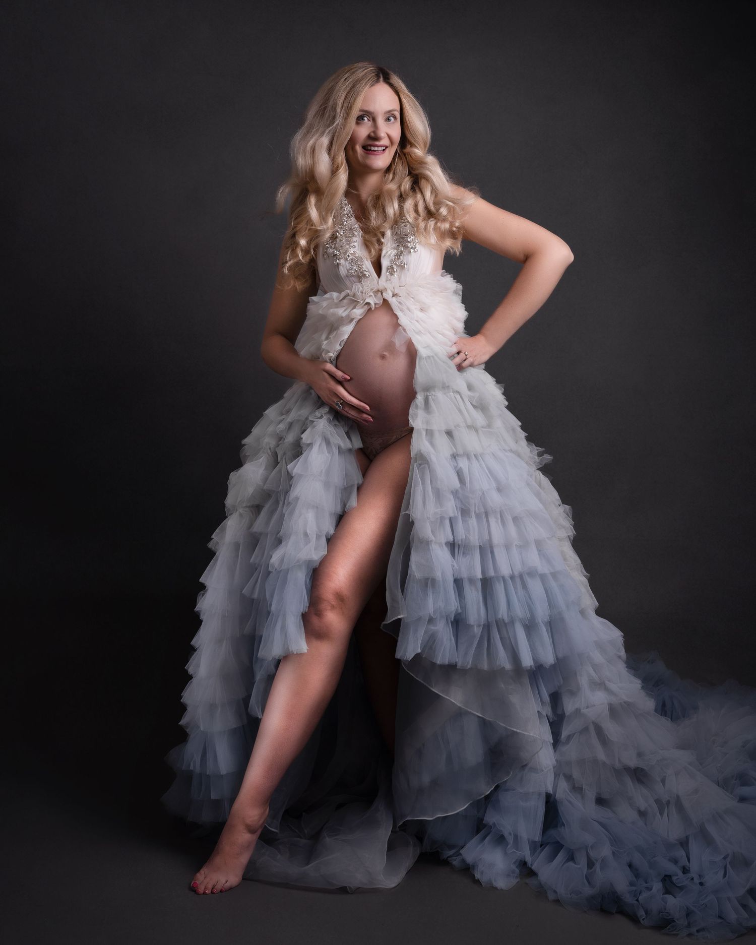 Maternity photo featuring a flowing white ruffled gown with dramatic layers against a dark background.