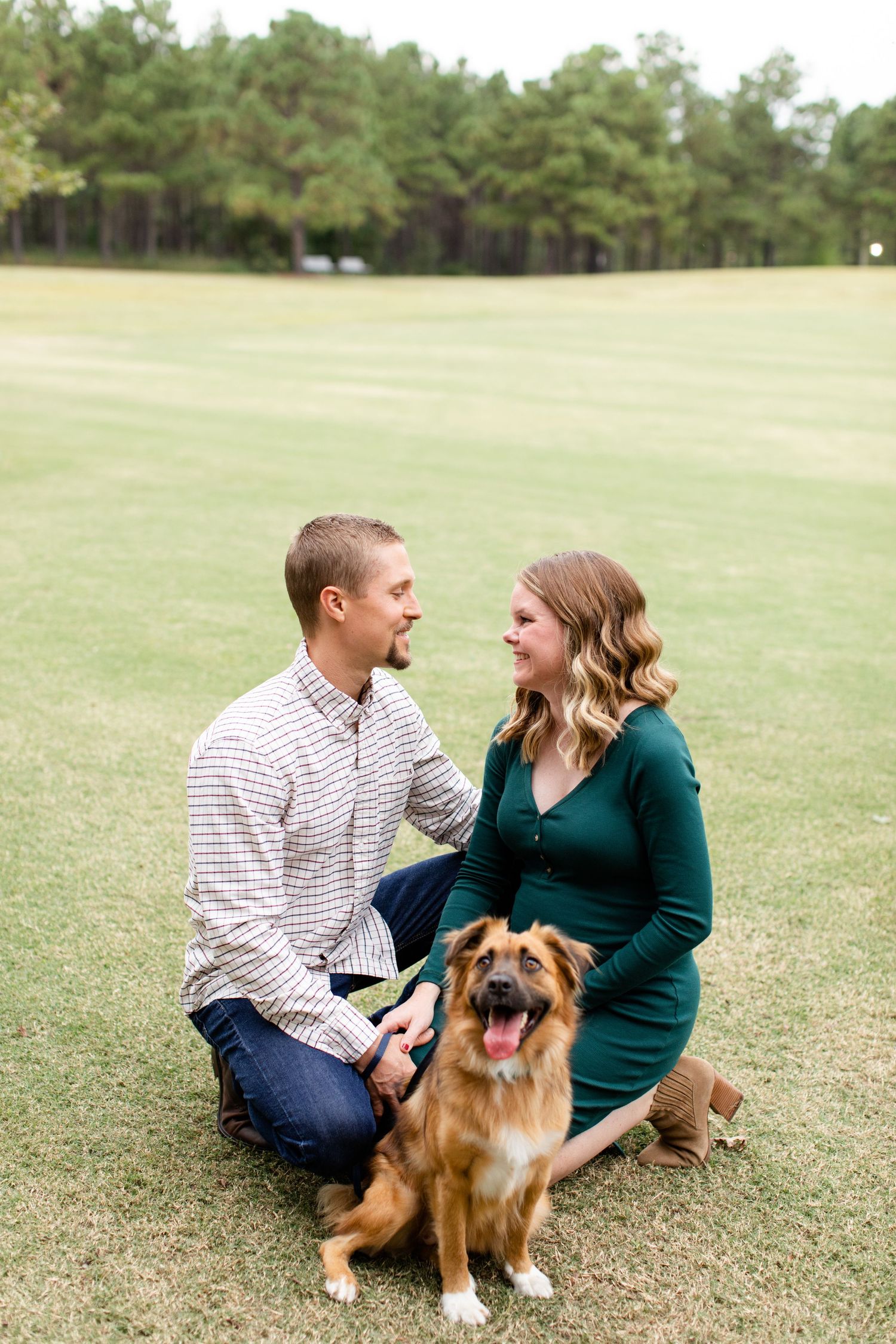 Happy couple and their dog share a moment during maternity photo session on grassy field.