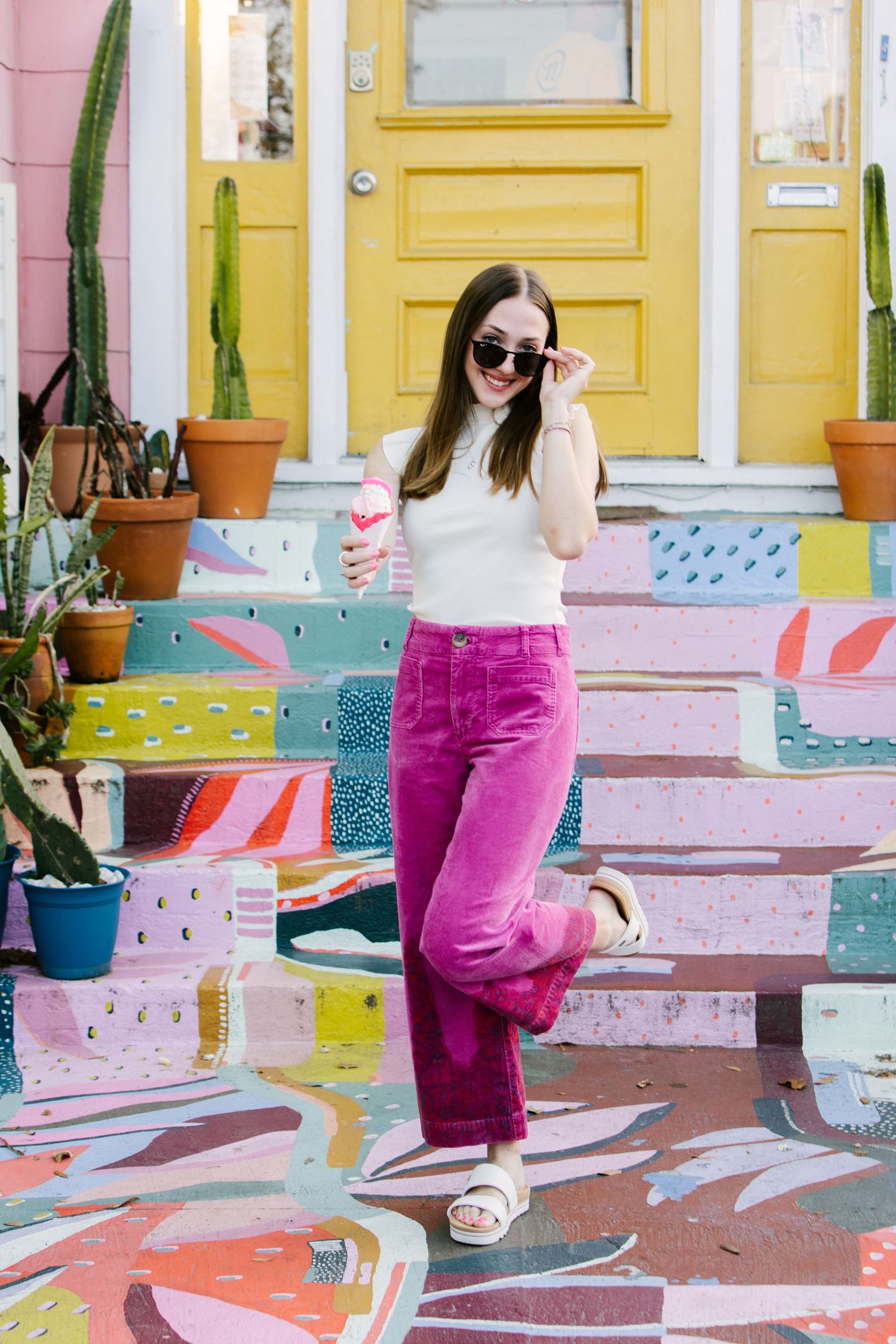 Stylish pose on colorful painted steps wearing bright pink pants and sunglasses.