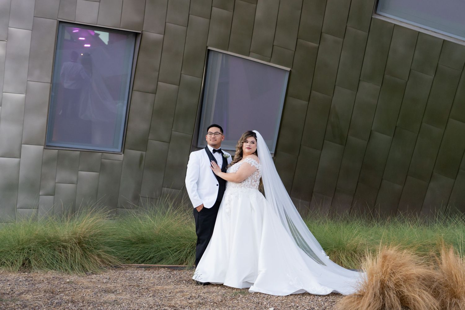 Wedding couple posing against modern architectural wall with geometric metallic panels.