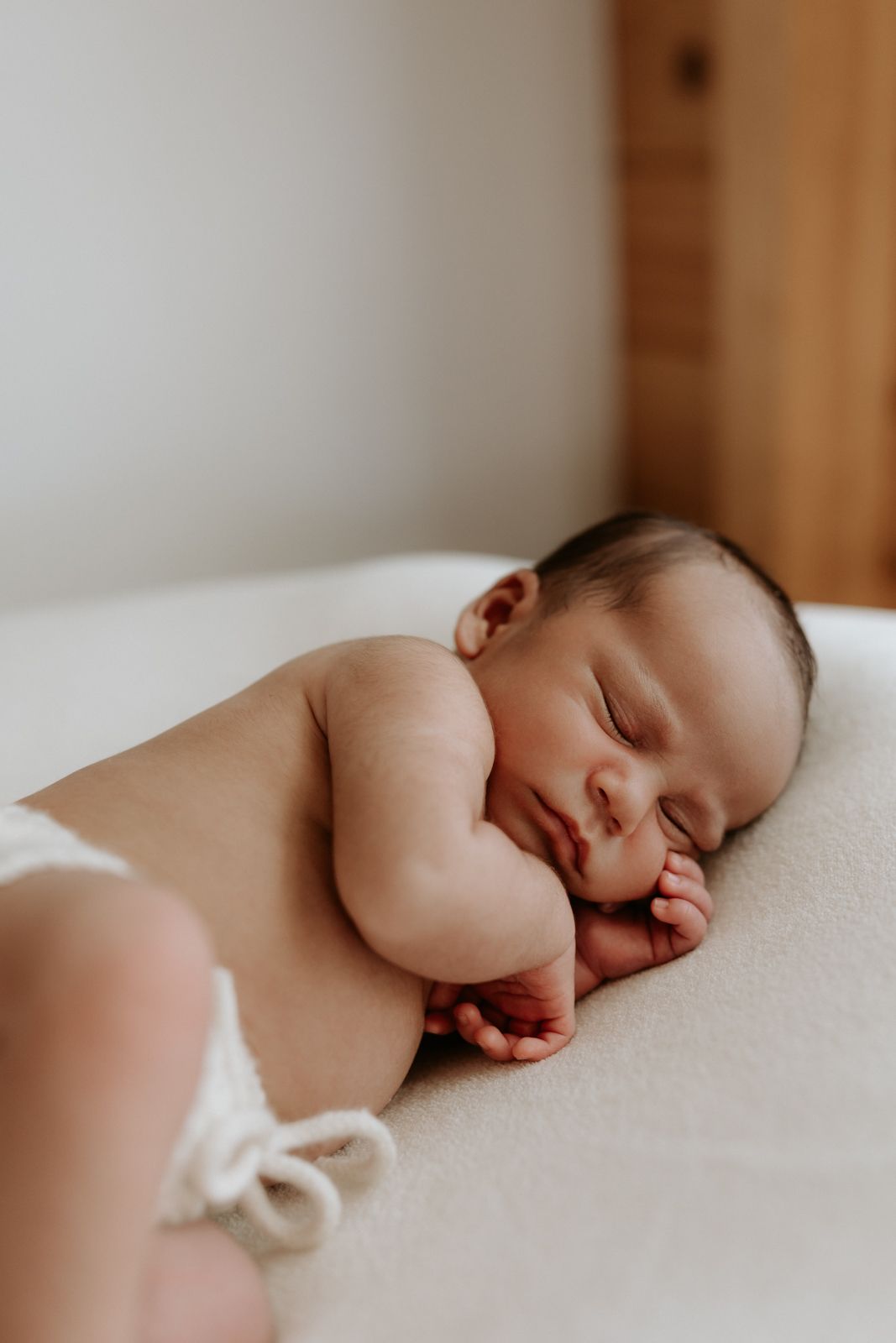Close-up of newborn sleeping peacefully on a cream knit blanket during an in-home newborn session. Westport NZ