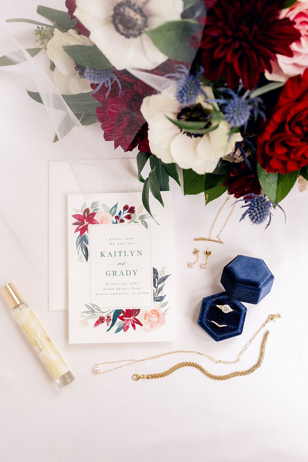Wedding invitation with floral design displayed with blue ring box and jewelry on white surface.