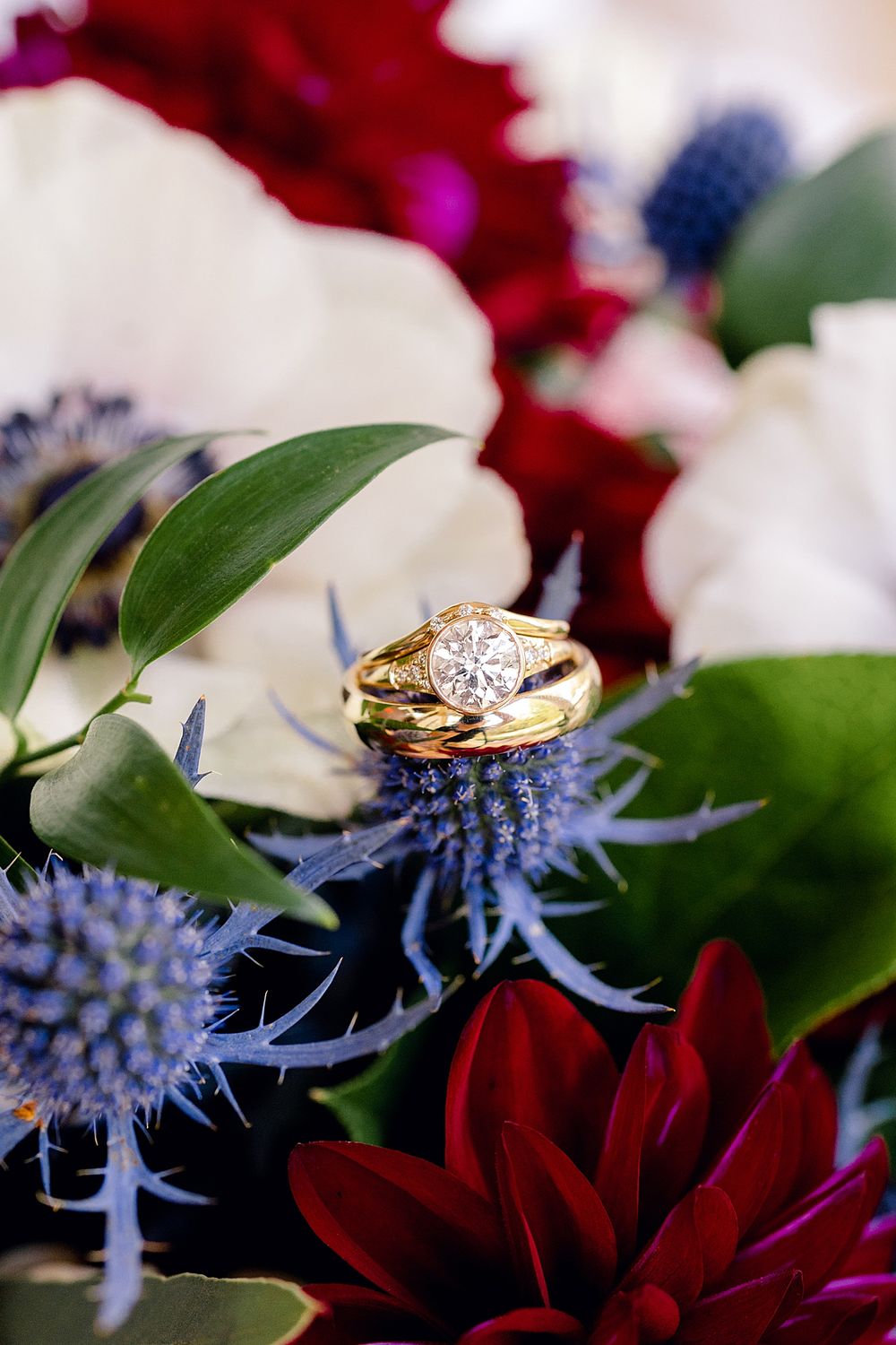 Diamond wedding rings nestled among red dahlias and blue thistle flowers.