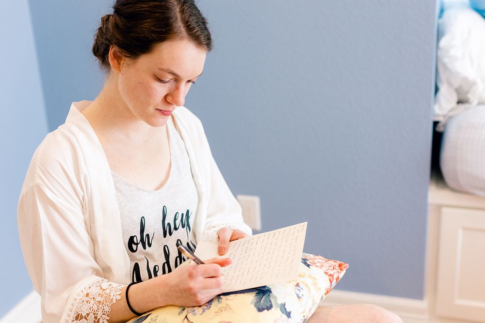 Person in white robe writing in notebook while sitting indoors.