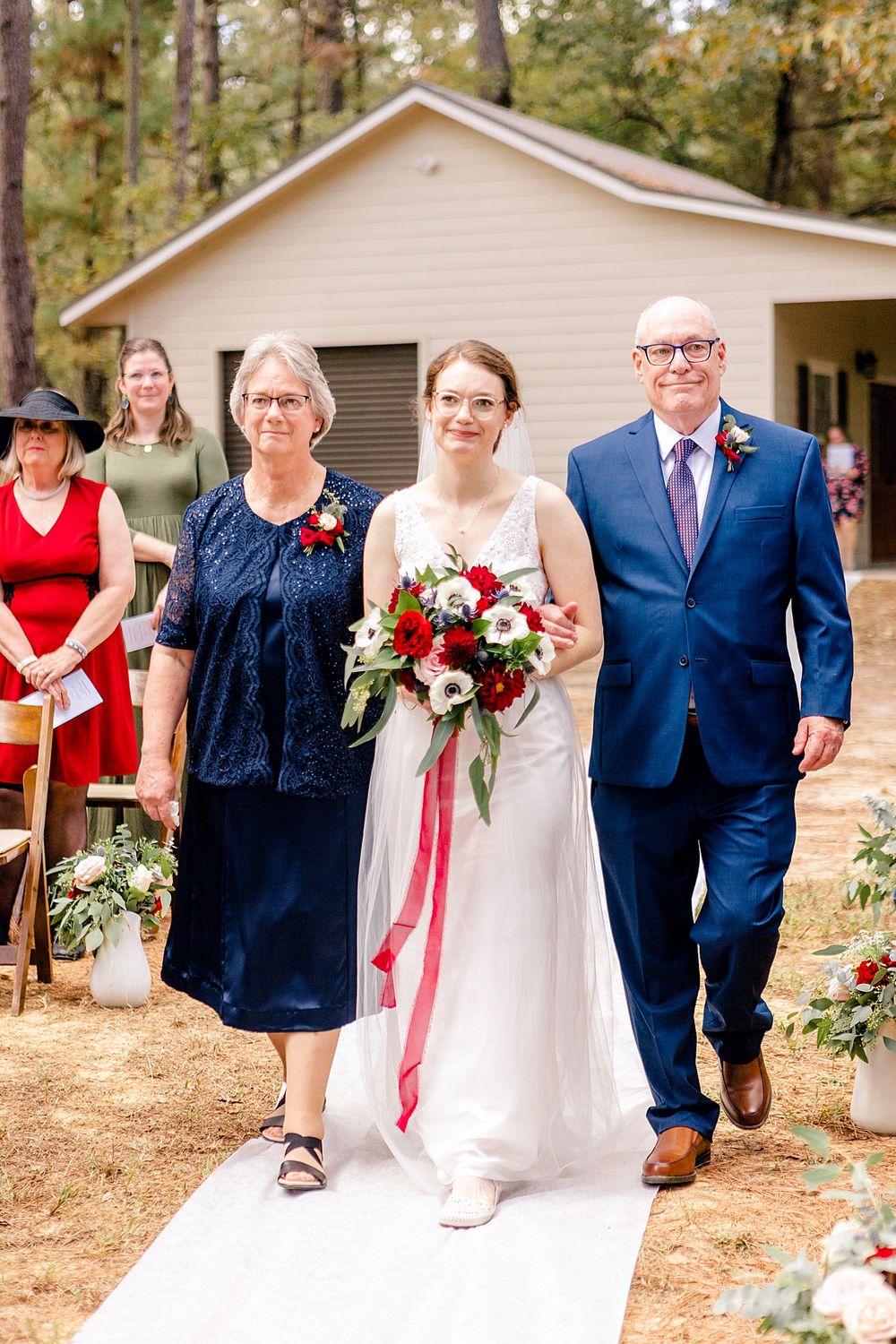 A wedding party walking down an outdoor aisle with pine trees in the background.