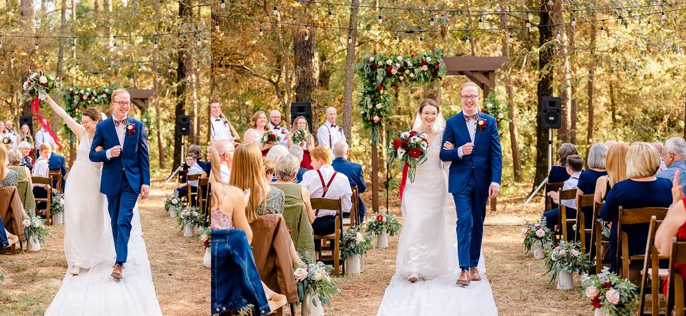 Wedding celebration in wooded setting with guests seated along aisle decorated with flowers.