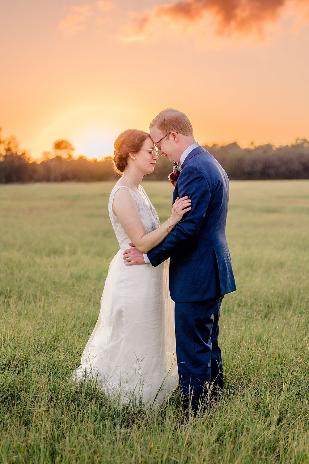 Intimate wedding portrait at sunset in open field with orange sky.