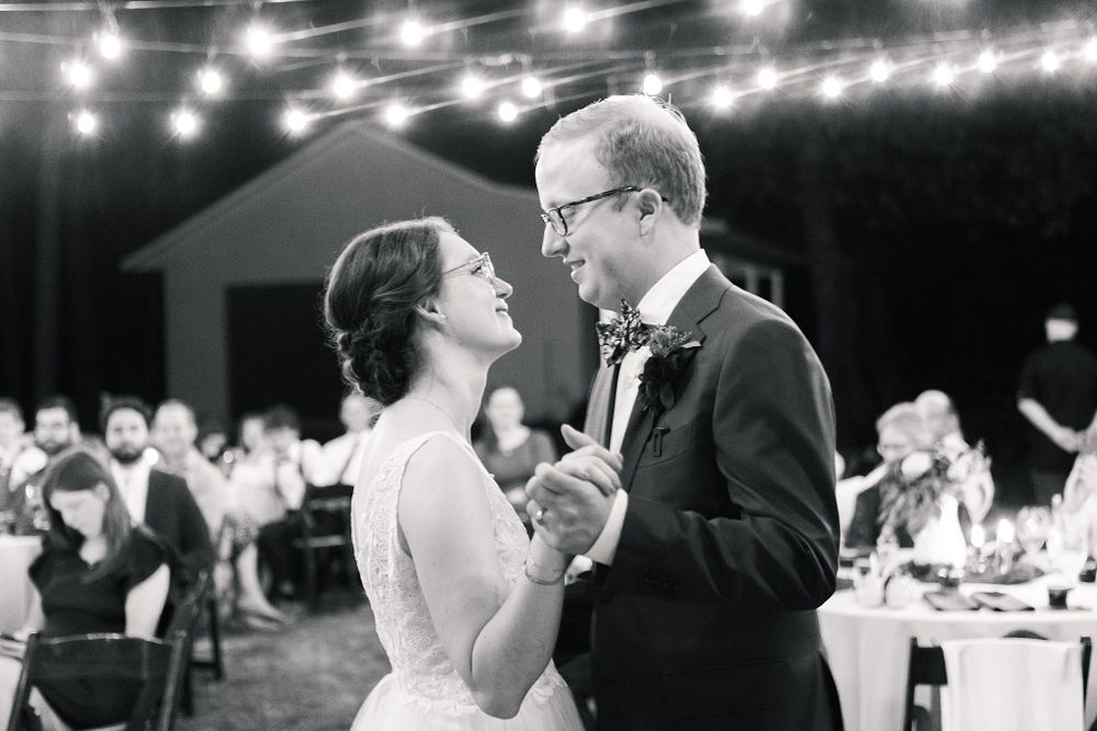 A couple shares their first dance at an evening wedding reception under twinkling lights.