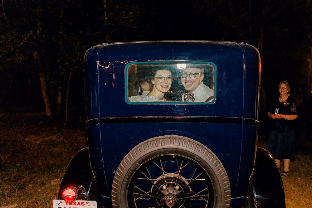 A vintage blue car displays a photograph in its rear window at night.