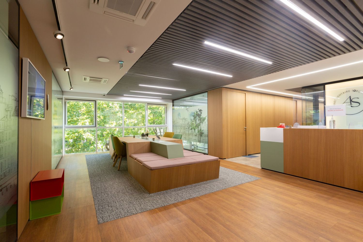 Modern medical office waiting room with wood floors and large windows overlooking greenery.
