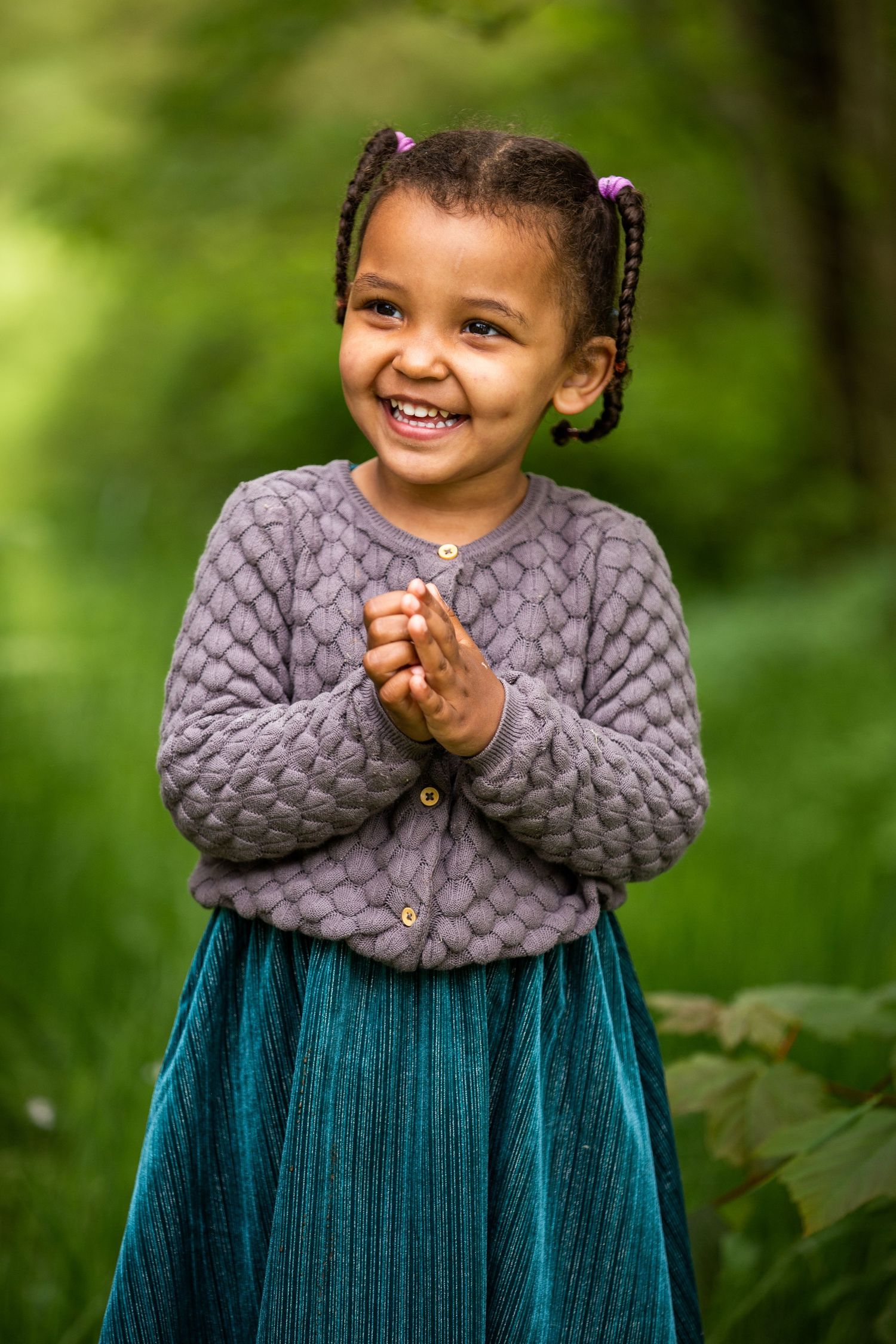 Joyful expression in grey sweater and teal skirt against green background.
