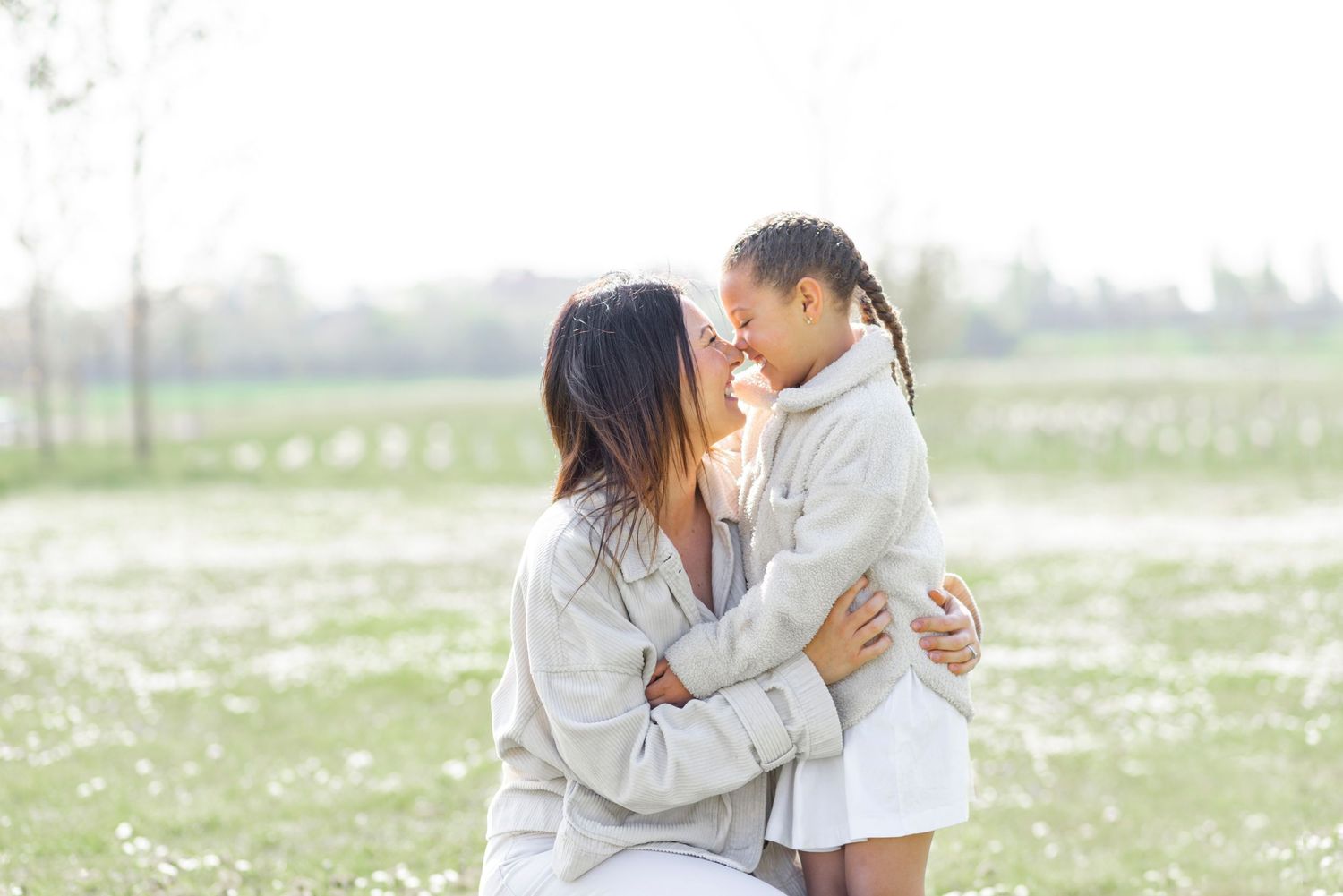 Two people share a tender embrace while standing in a field of white wildflowers on a bright sunny day.