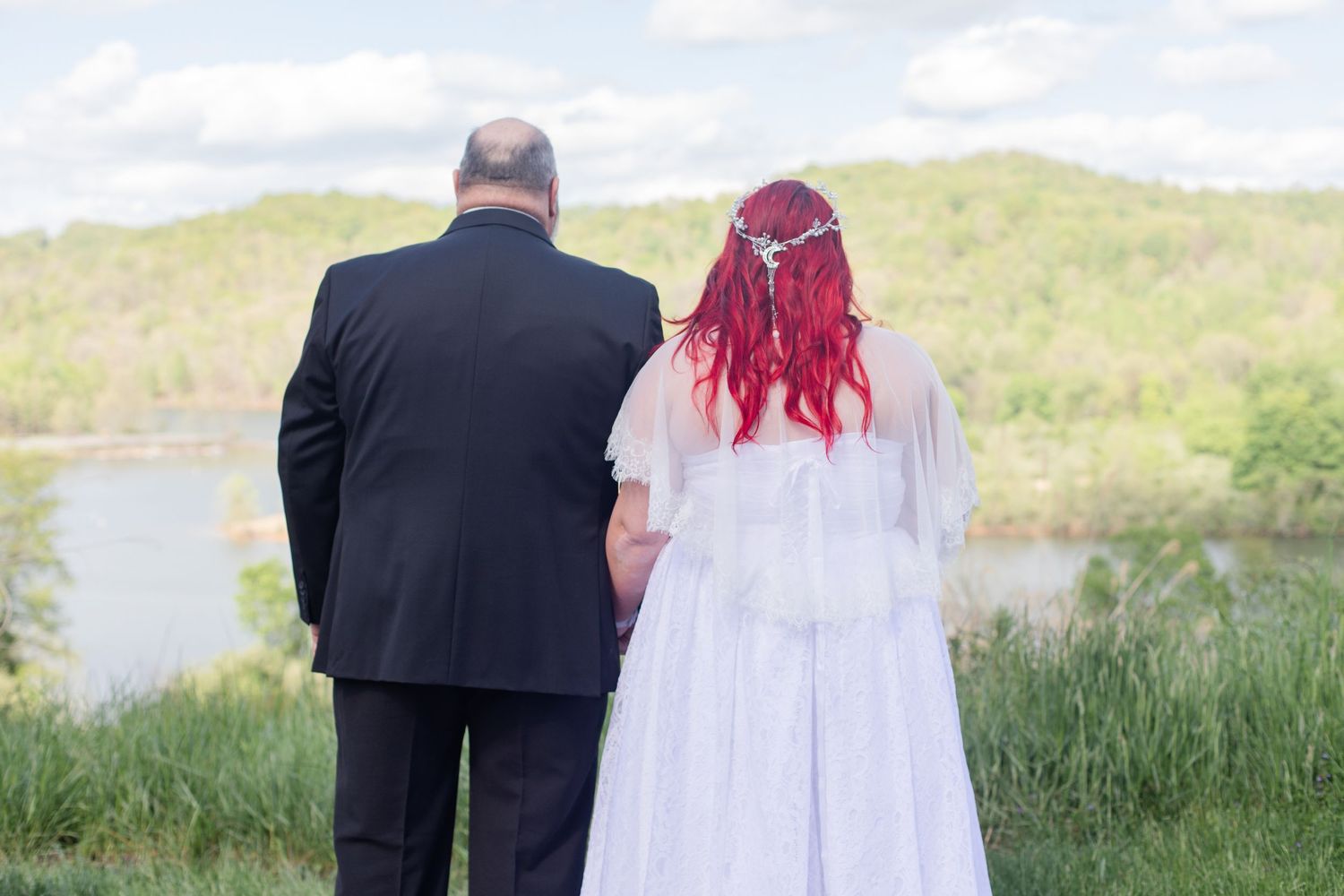 Wedding couple walking together in a scenic outdoor setting with rolling hills and water views.