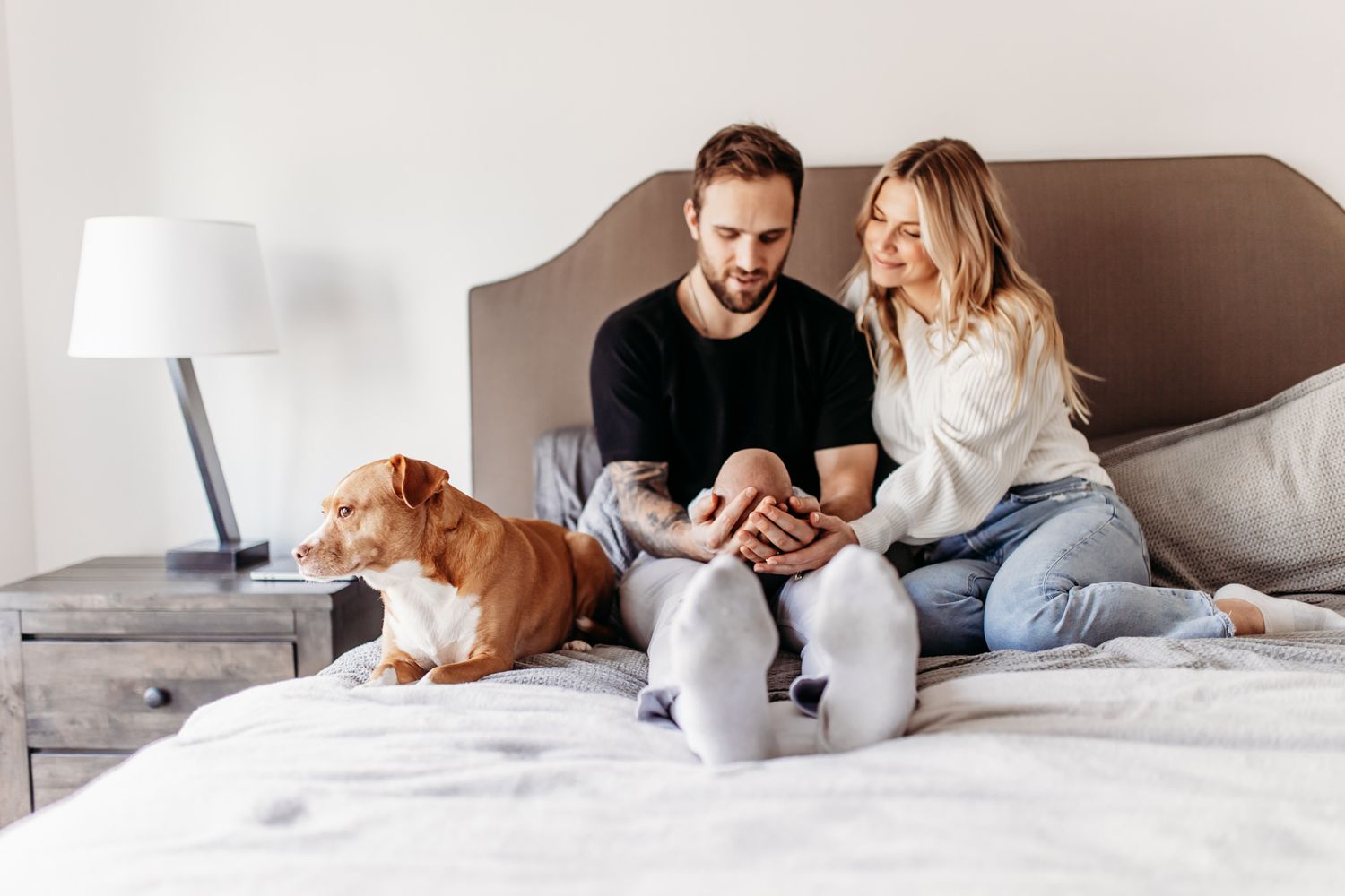 Couple sits on bed with dog while looking at something together.