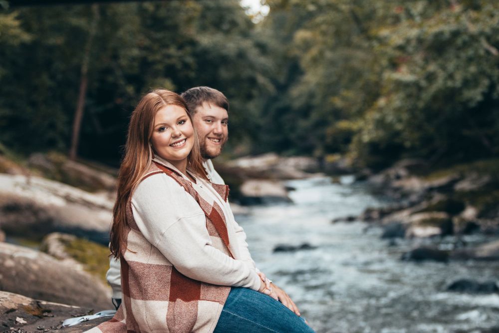 A couple enjoys a tender moment beside a rushing stream in a wooded setting.