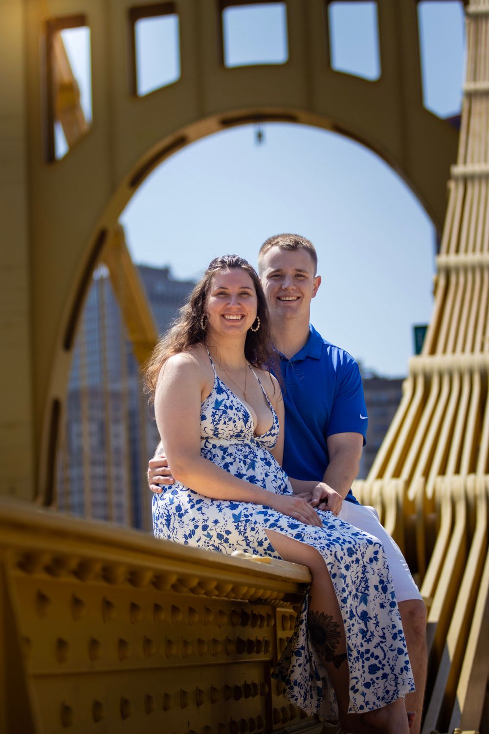 Couple poses under golden bridge arch in coordinated blue and floral outfits.